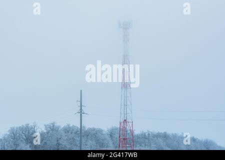 Zellenturm im Winter Nebel Nahaufnahme. Telekommunikationstürme mit Funkantennen in RIME. Antennen für die Informationsübertragung, mobile Kommunikation Stockfoto