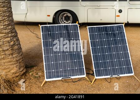 Zwei mobile Sonnenkollektoren neben einer Palme mit Ein großes Wohnmobil hinter Stockfoto