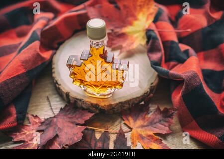 Ahornsirup-Geschenkflasche in roten Ahornholzblättern für Touristen-Souvenir. Canada Grade EINE bernsteinsüße natürliche Flüssigkeit aus Québec Sugar Shack Ahornbäumen Stockfoto