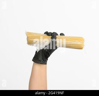 Weibliche Hand in einem schwarzen Handschuh hält einen transparenten Beutel mit Spaghetti Stockfoto