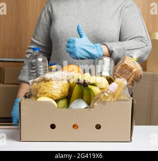 Frau in Handschuhen sammelt immer wieder Lebensmittel, Früchte und Dinge und einen Karton Stockfoto