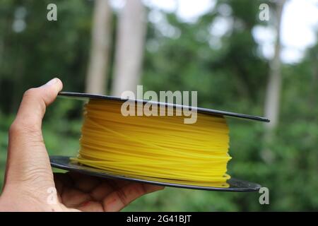 Drucker-Filament aus Bio-Kunststoff in Hand mit der Natur auf dem Hintergrund gehalten, um Konzept der Umweltfreundlichkeit zu zeigen, da Material biologisch abbaubar ist Stockfoto