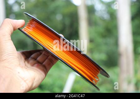 3D-Druckmaterial aus Biokunststoff. PLA Filament orange Spule in der Hand. Stockfoto