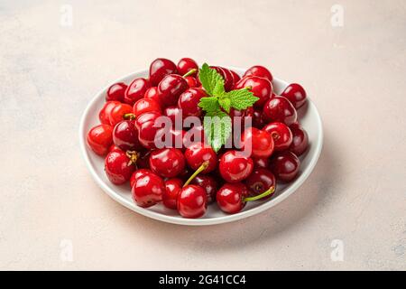 Rote, saftige Kirschen und Minze auf einem Teller auf rosa Hintergrund. Seitenansicht, Nahaufnahme. Stockfoto