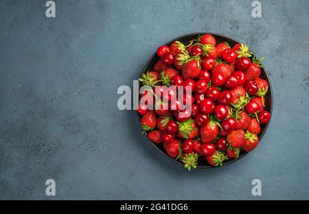 Ein Teller mit Kirschen und Erdbeeren auf grau-blauem Hintergrund. Draufsicht, horizontal. Speicherplatz kopieren. Stockfoto