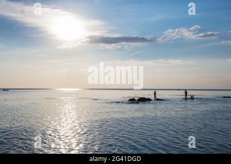 Silhouette von zwei Fischern und Hunden, die auf Felsen im Wasser vor Ong lang Beach, Ong lang, Phu Quoc Island, Kien Giang, Vietnam, Asien Stockfoto