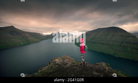 Frau am Aussichtspunkt Klakkur in der Nähe von Klaksvik auf der Insel Bordaoy mit Blick auf Klasoy und Kunoy bei Sonnenuntergang, Färöer-Inseln Stockfoto