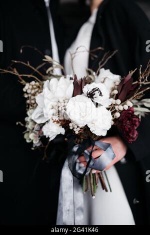 Nahaufnahme eines weißen Bouquets mit Seidenbändern, auf schwarzem Hintergrund, in den Händen der Braut. Hochzeit in Island. Stockfoto