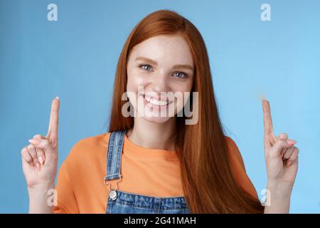 Taille-up charismatische gut aussehende europäische Rotschopf Frau lächeln aufrichtig gerne zeigen Weg zeigen nach oben Zeigefinger glücklich Hilfe Stockfoto