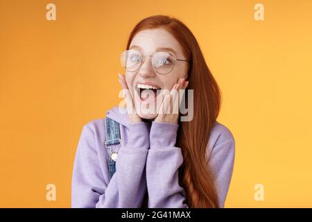 Aufgeregt glücklich lächelnd breit rothaarige Freundin Tropfen Kiefer grinsend begeistert Blick links erstaunt berühren Wangen reagieren genial s Stockfoto