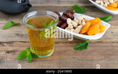 Obstschale mit Datteln, Pistazien und getrockneten Aprikosen mit Teeglas auf Holzboden. Speicherplatz kopieren. Stockfoto