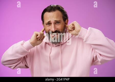 Unzufrieden genervt erwachsenen bärtigen Mann fühlen sich unwohl abgelenkt laut schrecklichen Lärm runzelig knarren hören schlechten Musiker Gitarre spielen Stockfoto