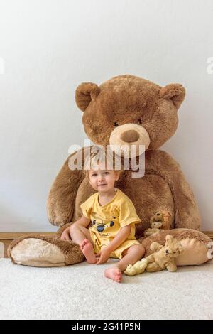 Süßer, fröhlicher Junge, der mit seinem riesigen Teddybären spielt, drinnen zu Hause Stockfoto