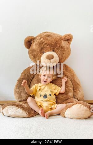 Süßer, fröhlicher Junge, der mit seinem riesigen Teddybären spielt, drinnen zu Hause Stockfoto