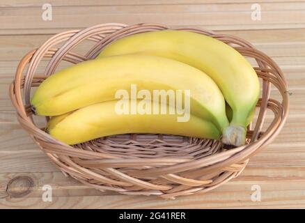 Ein hochwinkliger Schuss reifer Bananen in einem Strohkorb auf einem Holztisch Stockfoto