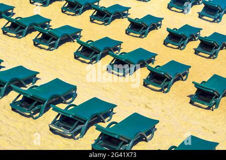 Reihen von kostenlosen grünen Sonnenliegen an einem leeren Sandstrand. Geschlossen Urlaubskonzept oder Nebensaison Stockfoto