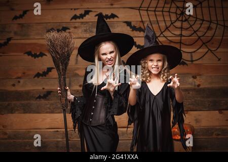 Halloween-Konzept - fröhliche Mutter und ihre Tochter in Hexenkostümen feiern Halloween posieren mit geschwungenen Kürbissen über BA Stockfoto