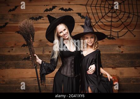 Halloween-Konzept - fröhliche Mutter und ihre Tochter in Hexenkostümen feiern Halloween posieren mit geschwungenen Kürbissen über BA Stockfoto