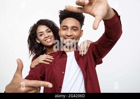 Glückliche junge afrikanische amerikanische Paar durch einen Finger Rahmen und lächelnd beim Stehen auf weißen isoliert. Stockfoto