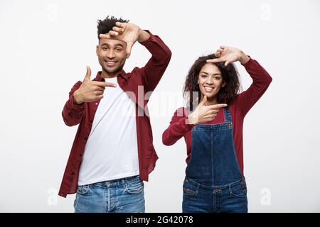 Glückliche junge afrikanische amerikanische Paar durch einen Finger Rahmen und lächelnd beim Stehen auf weißen isoliert. Stockfoto
