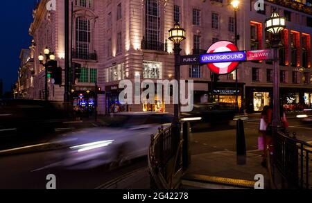 Abendliche Verkehrsaufnahme und das klassische Schild der Londoner U-Bahn. Gedreht im Piccadilly Circus in London, Großbritannien. Stockfoto