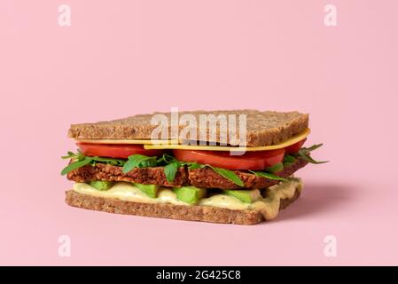 Gesundes fleischloses Sandwich mit veganen Zutaten und frischem Gemüse. Sandwich auf pflanzlicher Basis mit geräuchertem Tofu, veganem Käse, Avocado, Remoulade, Tomate Stockfoto