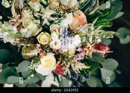 Brautstrauß aus weißen und cremefarbenen Rosen, Ästen von Eukalyptusbäumen, protea, Eryngium und Delphinium Stockfoto