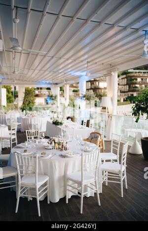 Empfang am Tisch für Hochzeitsessen. Runder Banketttisch mit weißer Tischdecke und weißen Chiavari-Stühlen. Hochzeit unter dem Zelt. Stockfoto