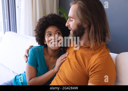 Ein glückliches, vielfältiges Paar, das auf dem Sofa sitzt und umarmt und lächelt Stockfoto