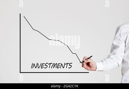 Businessman zeichnet ein abnehmendes Liniendiagramm mit dem Wort Investitionen. Sinkende Unternehmensinvestitionen. Stockfoto