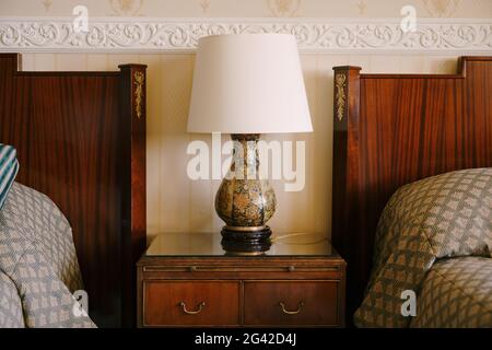 Nachttischlampe am Nachttisch. Raffiniertes und reiches Interieur. Nachttisch aus Holz neben zwei Betten. Stockfoto