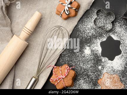 Sternförmige gebackene Lebkuchen, die mit Puderzucker bestreut wurden Ein schwarzer Tisch Stockfoto
