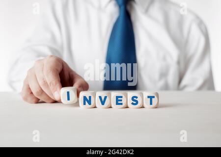 Geschäftsmann arrangiert Holzwürfel mit dem Wort Invest. Entscheidung über finanzielle Investitionen. Stockfoto