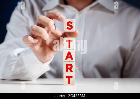 Der Mensch legt einen Würfel mit dem Wort „Start“ auf gestufte Holzwürfel. Geschäftskonzept. Stockfoto