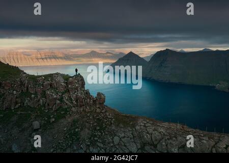 Wanderer bei Hvithamar in der Nähe der Stadt Gjogv auf der Färöer Insel Eysturoy mit Panoramablick auf den Fjord bei Sonnenuntergang Stockfoto