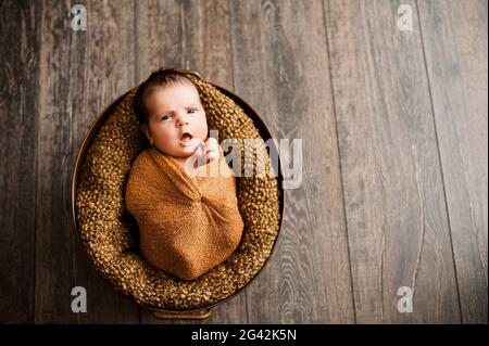 Das Mädchen in einem braunen Wrap gähnt bei einem neugeborenen Fotoshooting Stockfoto