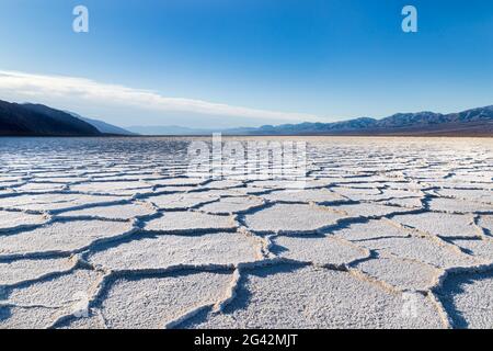 Sonnenaufgang über dem Badwater Basin, Death Valley, Kalifornien. Sunburst über den fernen Bergen; der Beckenboden ist mit weißen Salzablagerungen bedeckt. Stockfoto