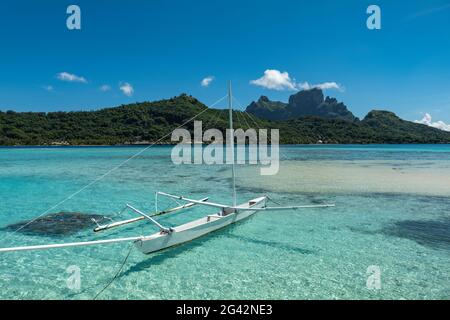 Outrigger-Kanu am Strand im Sofitel Bora Bora Private Island Resort in der Bora Bora Lagune mit Mount Otemanu in der Ferne, Bora Bora, Leeward Stockfoto