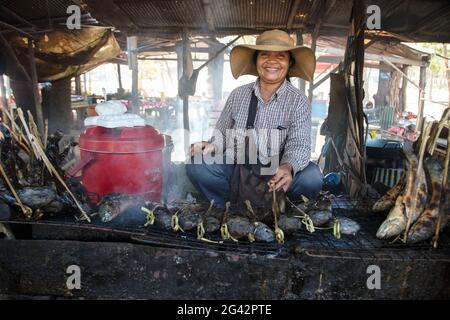 Fröhliche Frau mit gegrilltem Fisch an einem Street Food Stand auf dem Markt, Oudong (Udong), Kampong Speu, Kambodscha, Asien Stockfoto
