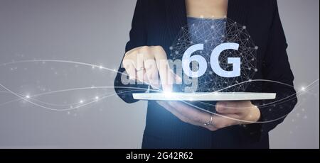 6G Network Internet Mobile Wireless Business. Weiße Tablette in Geschäftsfrau Hand mit digitalem Hologramm 6G Zeichen auf grau. Das Konzept des 6G-Netzwerks, hig Stockfoto