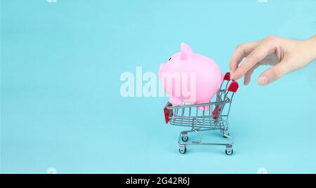 Hand-Touch Mini-Shopping-Trolley mit Sparschwein auf blauem Hintergrund. Geld sparen für den Verkauf des Jahres, Black friday Konzept Stockfoto