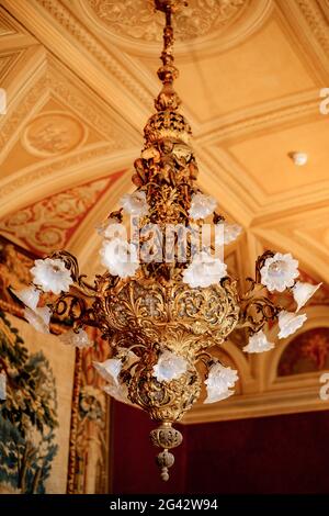 Ein alter riesiger goldener Kronleuchter mit weißen Farbtönen und Lampen, an der Decke mit Stuckverzierungen. Stockfoto