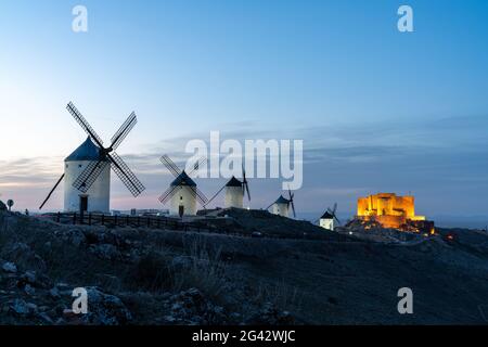 Ein Blick auf die Windmühlen und das Schloss von Consuegra in La Mancha in Zentralspanien bei Einbruch der Dunkelheit Stockfoto