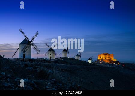 Ein Blick auf die Windmühlen und das Schloss von Consuegra in La Mancha in Zentralspanien bei Einbruch der Dunkelheit Stockfoto