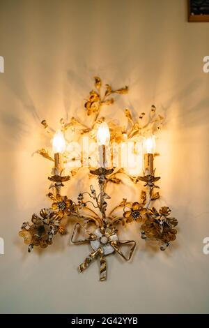 Goldene Stehleuchten mit drei Lampen, verziert mit Blumenmustern an der Wand. Inneneinrichtung einer alten Villa in Italien. Stockfoto