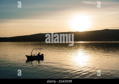 Ein Fischer fängt Fische im Meer vor dem Hintergrund eines Berges und Sonnenuntergang. Stockfoto