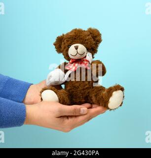 Lustiger Vintage brauner lockiger Teddybär mit aufgewickelter Pfote mit weißer Gaze-Bandage auf blauem Hintergrund Stockfoto