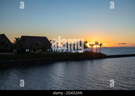 Silhouette von Villen eines Resorts und Kokospalmen am Eingang zum Hafen von Port Denarau bei Sonnenuntergang, Port Denarau, in der Nähe von Nadi, Viti Levu, Fidschi-Inseln, Stockfoto