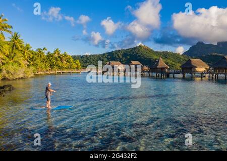 Luftbild des Menschen auf dem SUP Stand Up Paddle Board in der Bora Bora Lagune mit den Überwasser-Bungalows des Sofitel Bora Bora Private Island Resort dahinter, Vaitap Stockfoto