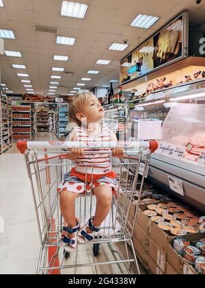 Budva, Montenegro - 10. juni 2020: Ein einjähriges Mädchen sitzt in einem Supermarkt-Trolley in der Fleischabteilung. Stockfoto